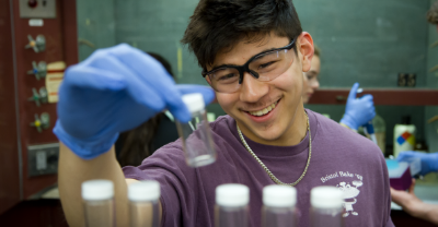 Student wearing safety glasses holding a vial in a laboratory.