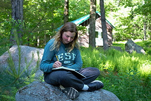 A girl siting on a rock and writing in a notebook