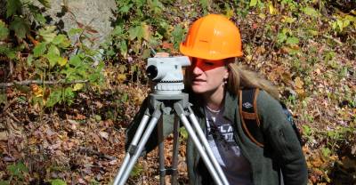 Student in a hard hat looking into a surveying instrument