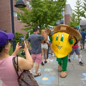 Woman taking a photo of young man high fiving Oakie the acorn mascot outside of Centennial Hall entrance