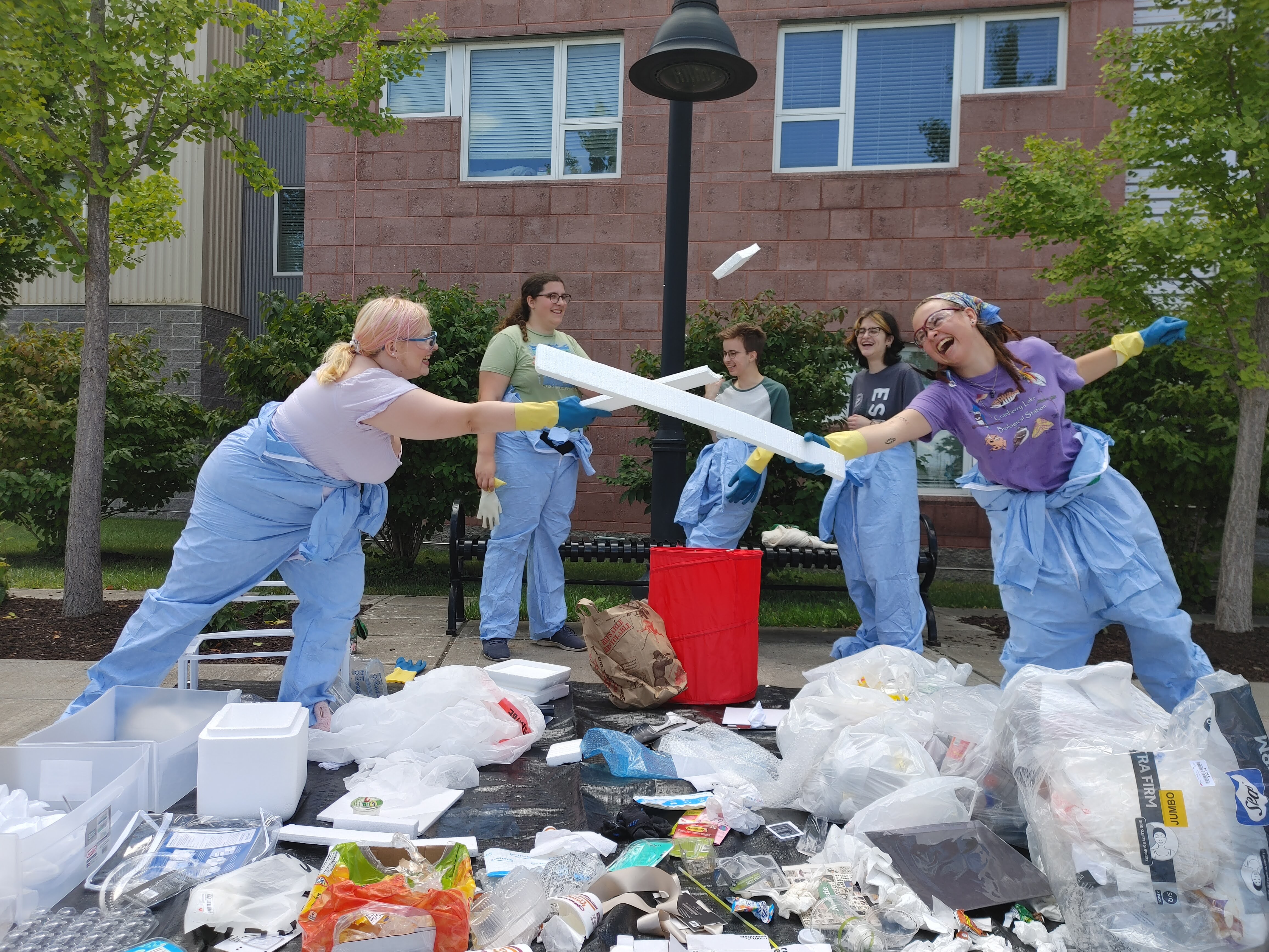 Two student EcoReps battle with styrofoam swoards, as other EcoReps look on smiling and laughing