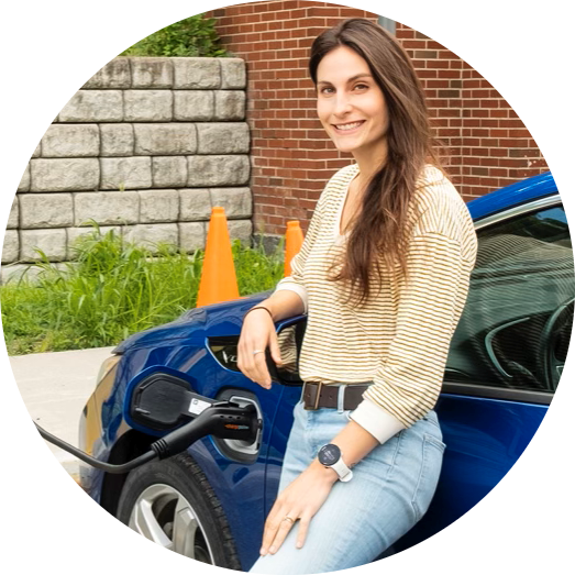 Sue Fassler leaning against a blue electric car being charged