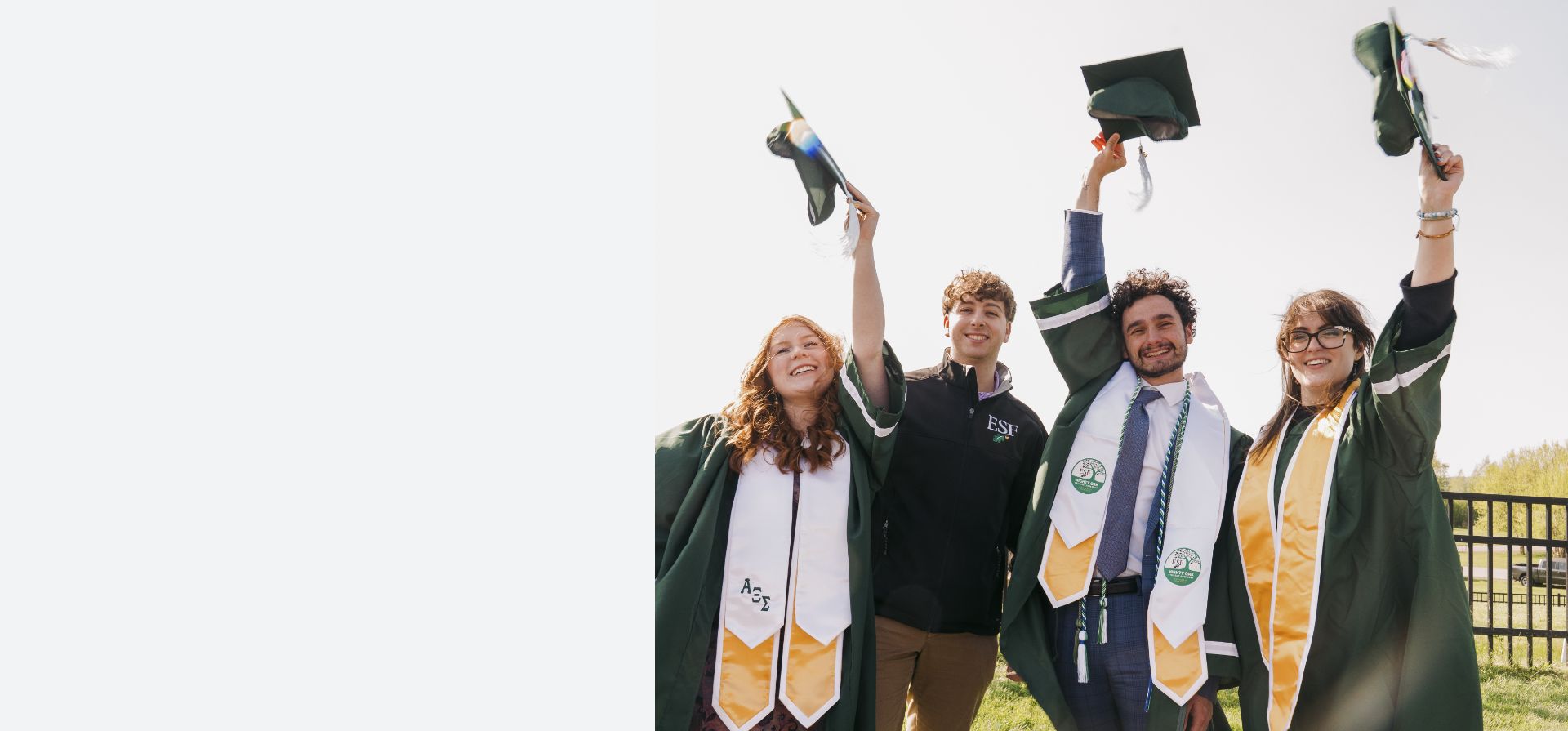 Graduates pose in robes with raised caps at Commencement