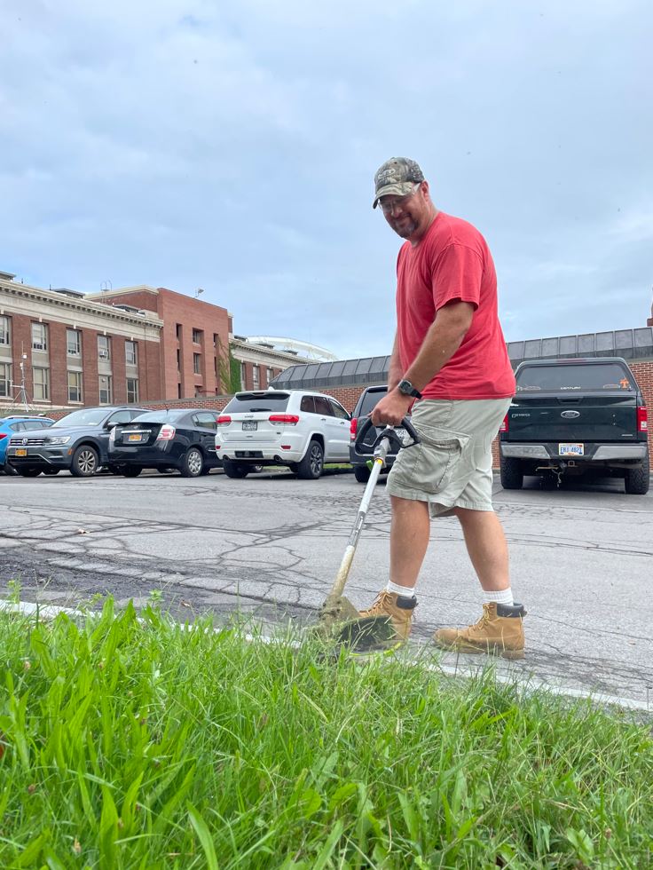 grounds crew member trims with electric string trimmer