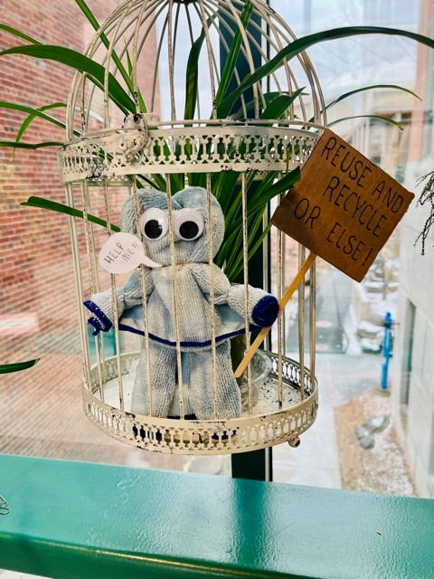 figure made from microfiber cloth holds a sign that says "reduce and recycle or else"