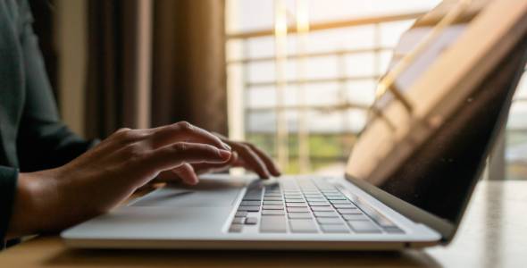 Photo of hands at a laptop computer keyboard next to a window.