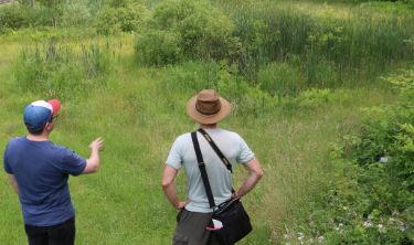 Students in a canoe and one student wading in a stream with net.