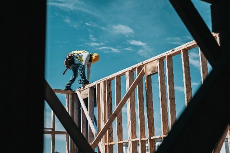 A man in yellow hard hat and tools belt working on a wooden frame