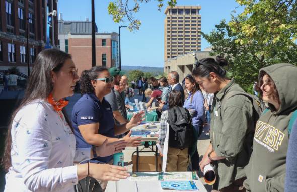Students interact with employers outdoors at tables.