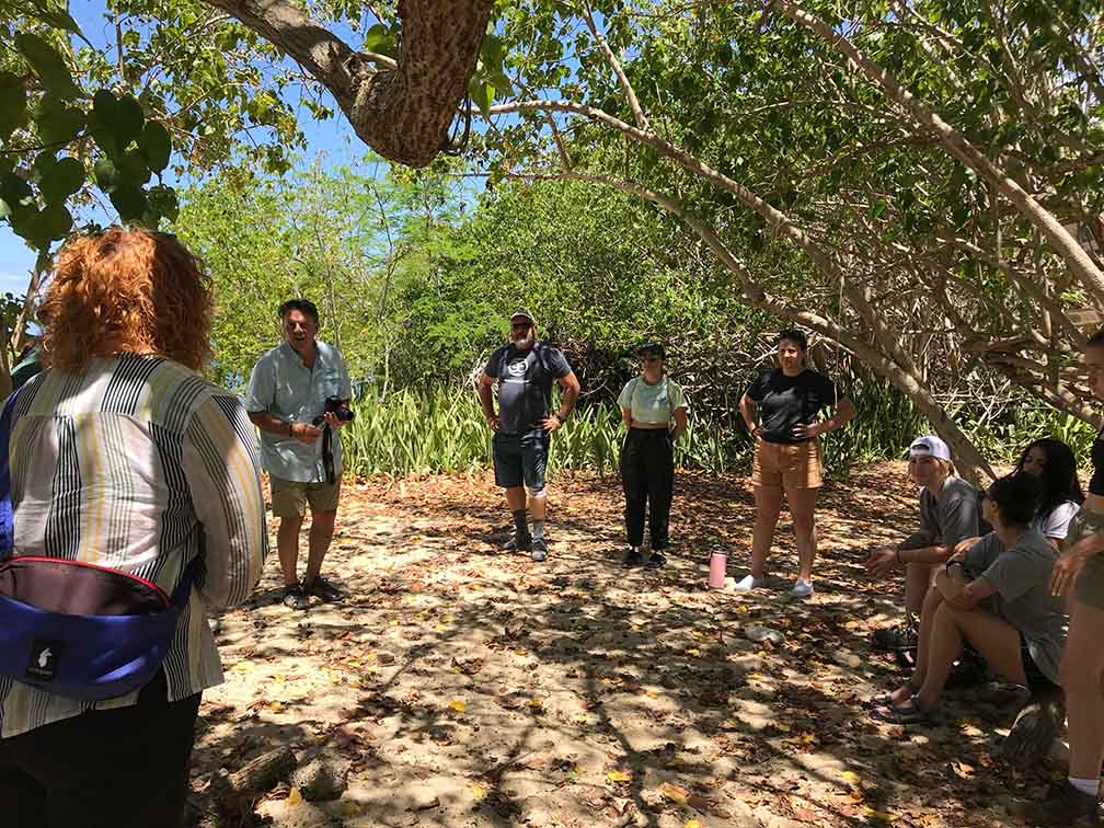 All the students are standing in a circle under a beautiful tree in Vieques, Puerto Rico. C C R D Advisor Mark Lichtenstein is addressing the students.