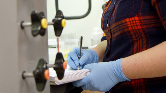 Student writing notes in a notebook at laboratory equipment.