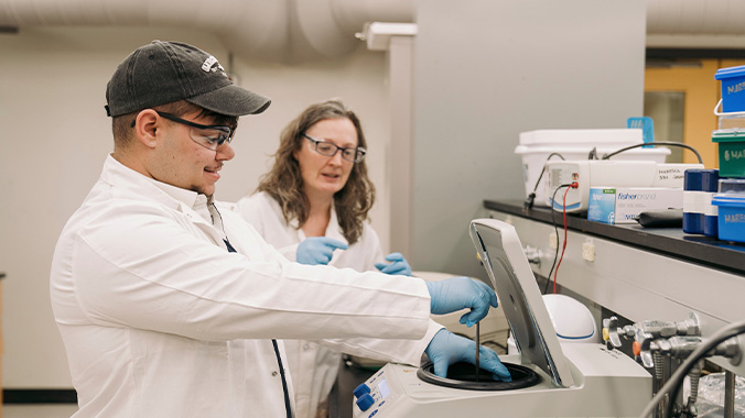 Faculty supervising a student using a centrifuge for biochemical samples.