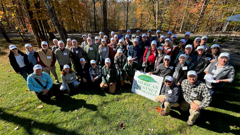 Members of the American Chestnut Foundation pose with a sign with their name with trees in the background.