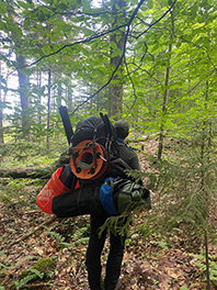 A guy walking in the woods with his camping gear and equipment