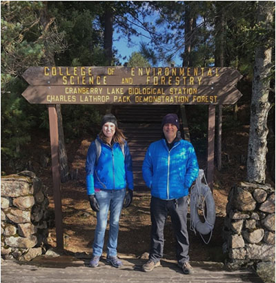 Kate Henderson and a guy standing infront of sign of College of Environmental Science and Forestry Cranberry Lake Biological Station Charles Lathrop Pack Demonstration Forest