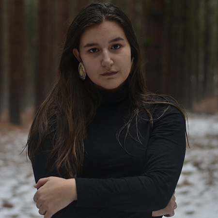 Skylar Kahentakwas Fetter in a black high neck shirt, her hands folded.