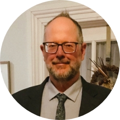 Headshot of Pete, white male glasses with salt and pepper beard in suit and tie