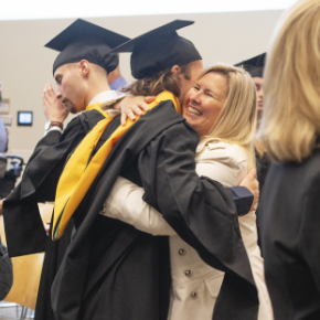 Students in cap and gown embraces a family member.