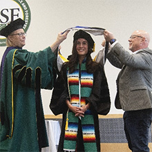 President Mahoney and another person putting a graduation sash on a student