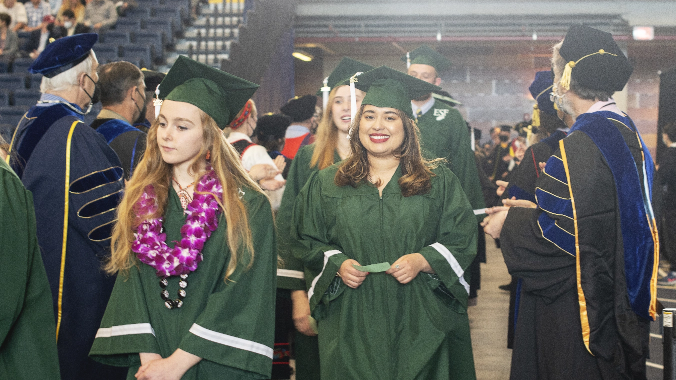 Students in graduation regalia walking into the hall