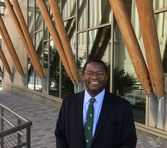 Provost of E S F Dr. Mukasa smiling infront of Gateway center. 