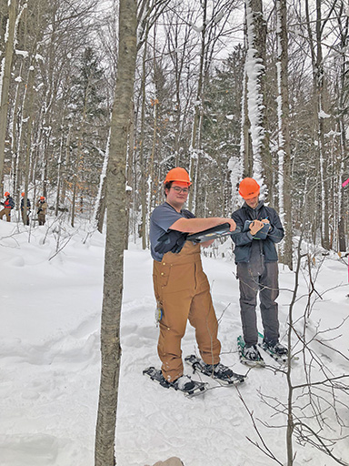 John Wise with a collegue on a survey. There is snow on the ground and both of them are wearing snow shoes and hard hats