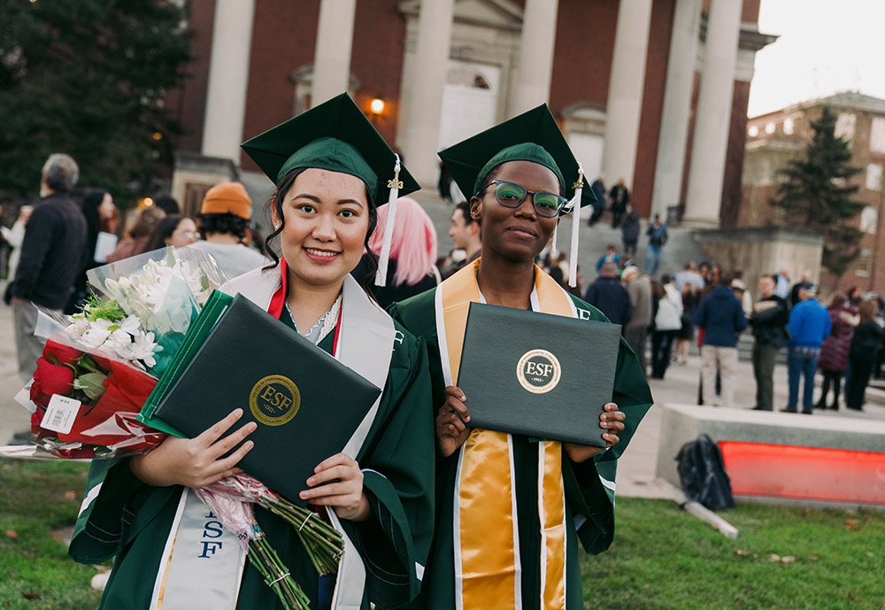 Two female students holding diplomas outside a university building