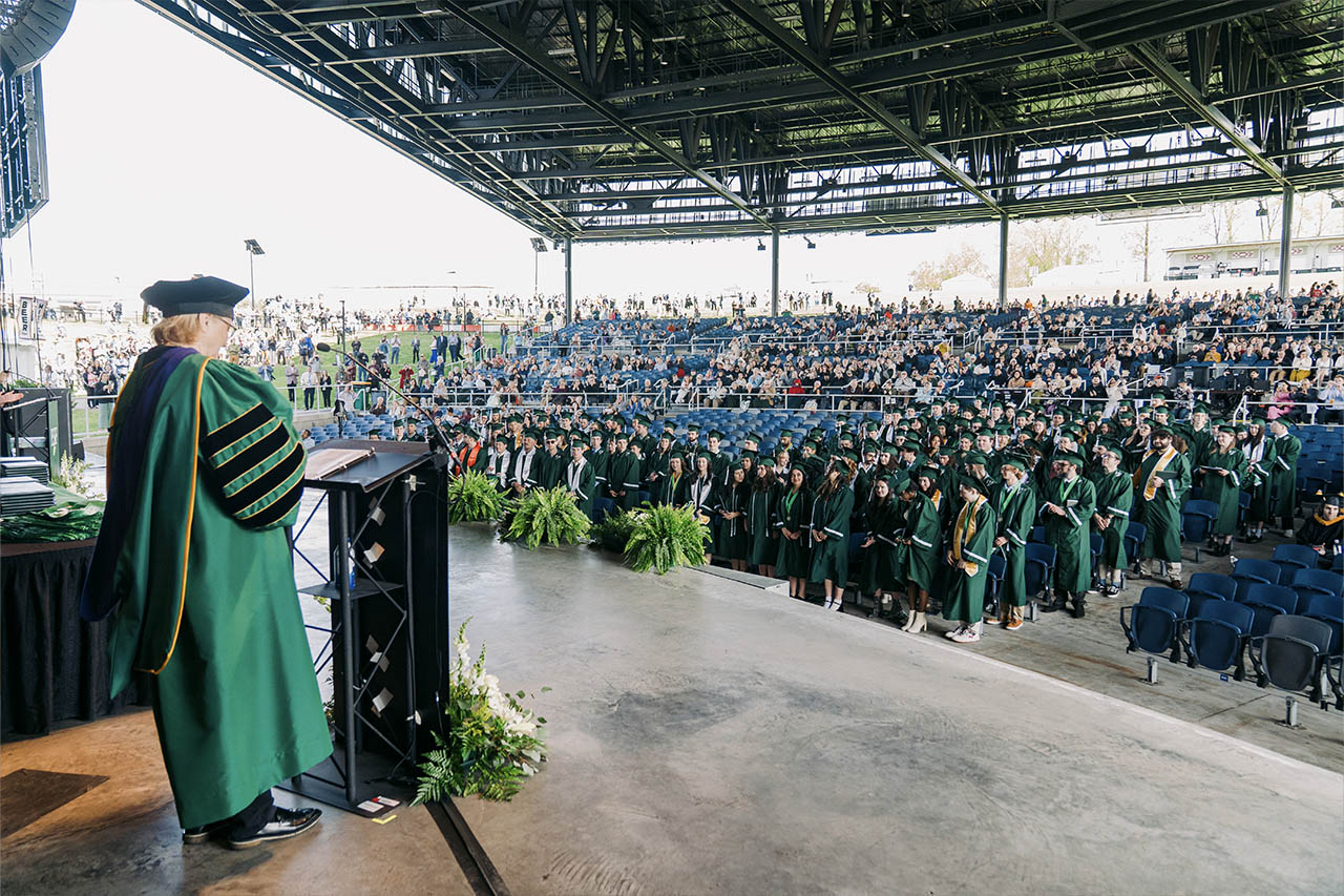 View from stage behand podium of seats filled with students in regalia and families behind