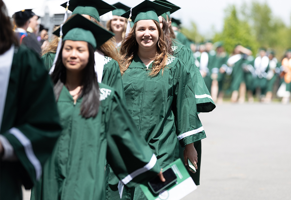 Female students being hooded by college president Joanie Mahoney (left) and male professor (right).