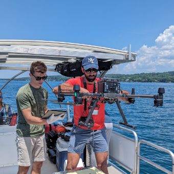 Two people standing using equipment aboard a boat.