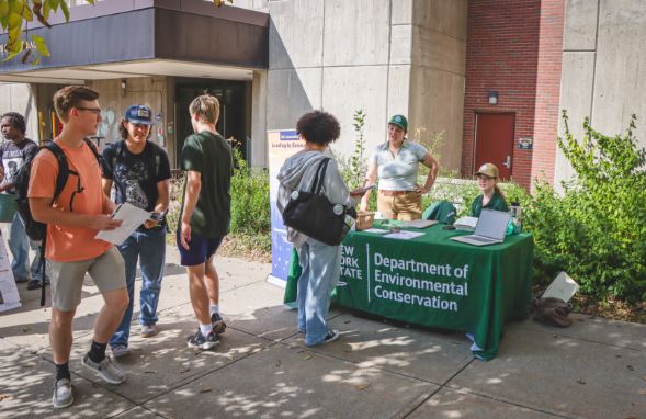 Students standing near a NYS DEC information table.