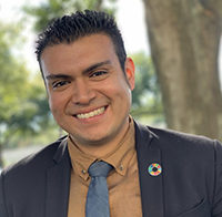 headshot of Jeff Benavides. He is smiling. He is wearing a brown shirt, grey tie, and a black jacket