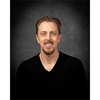 headshot of bremer against a greyish black background. He is wearing black tshirt