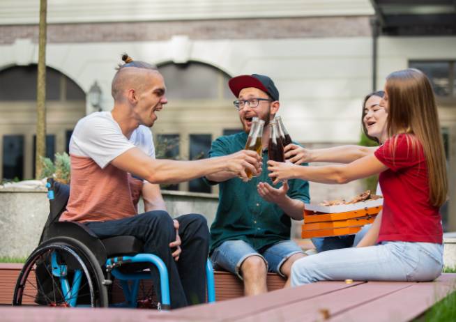 Group of people eating and drinking around a wall, with one in a wheelchair.