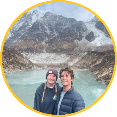 Two students standing in front of mountains and water in Nepal.