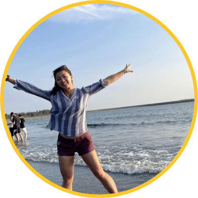 Student with arms spread standing at a shore with a group of students in the background.