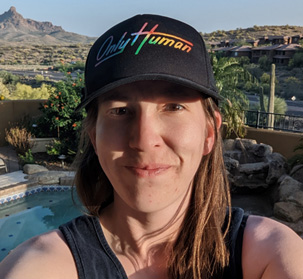 Mary banner selfie. She is wearing a black cap with the words only human. there are mountains in the background