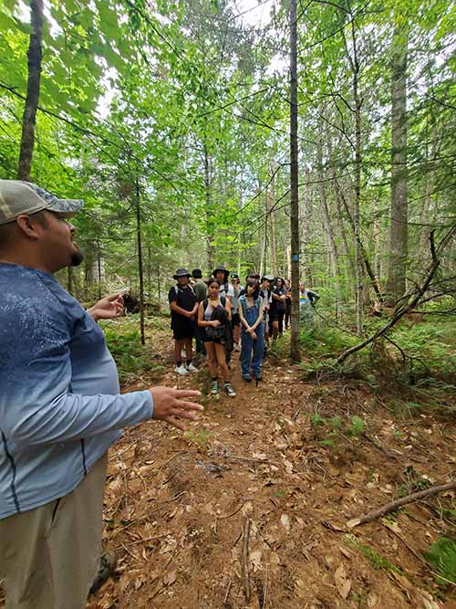 An instructor and students in the woods surrounded by trees.
