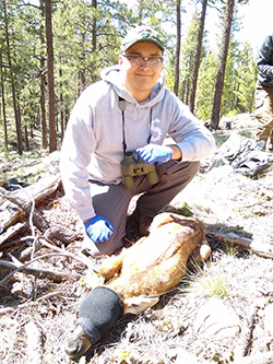 Ryan Masayesva kneeling on the ground in the woods