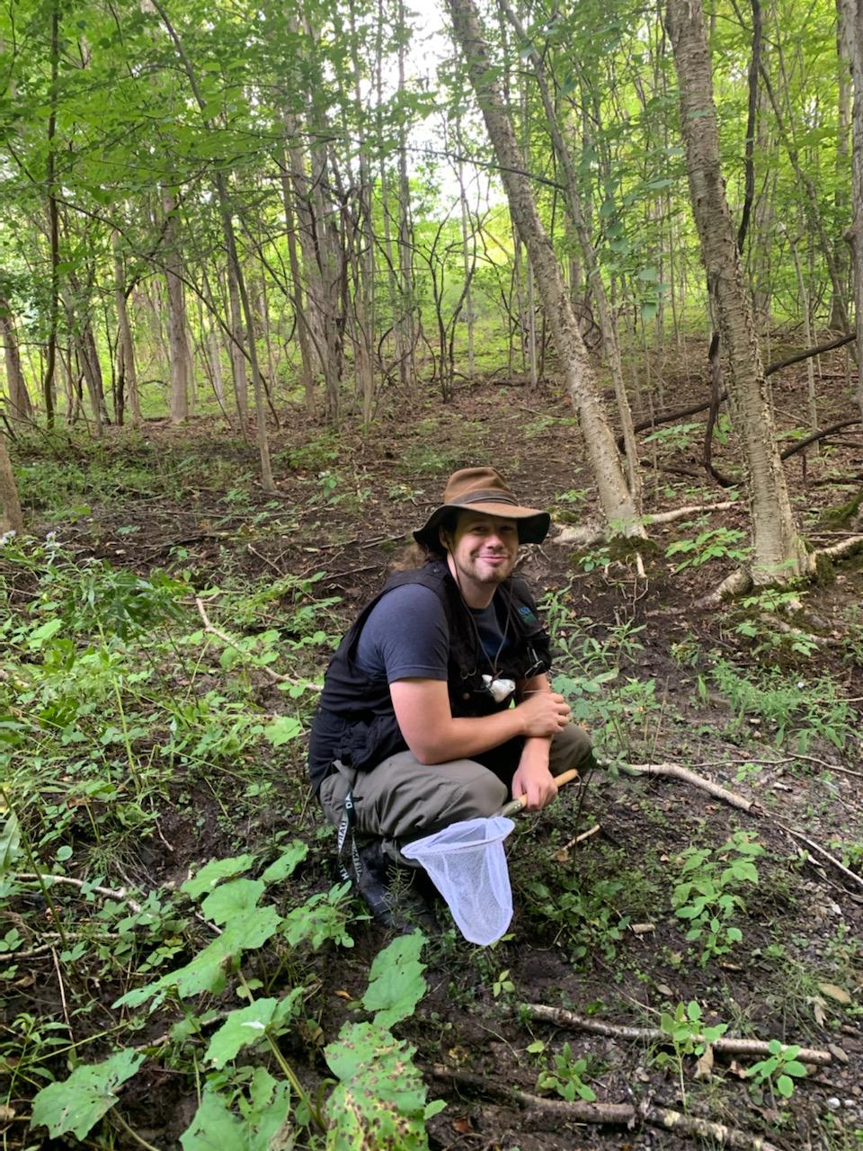 Spencer siting in the forest holding a net