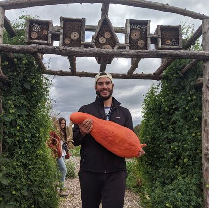 Justin Herne holding a big squash standing under a wooden gate