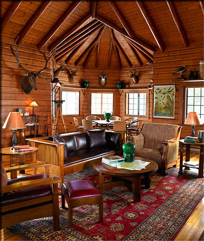 Arbutus lounge interior room. There are deer heads on the walls. A red carpet with some designs, a sofa with arm chairs on either side and a round coffee table in the middle