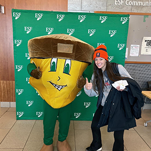 Woman with an SU hat on standing next to a giant yellow and green acorn. 