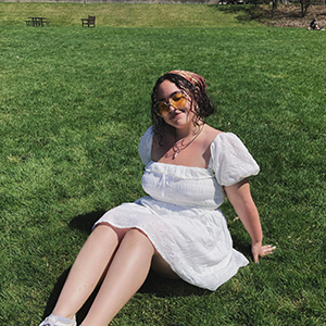 Woman in a white dress and sunglasses lounging on a green lawn. 
