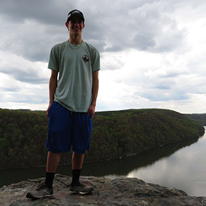 Man standing in nature with a large mountain behind him. 