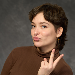Woman with a mullet flashing the peace sign against a grey backdrop. 