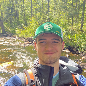 Man in a green hat with a brooke in the background. 