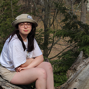 Woman sitting in nature with a white shirt on. 