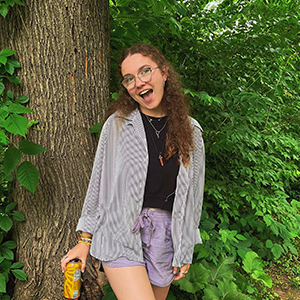 Woman in a black shirt standing with a tree in the background. 