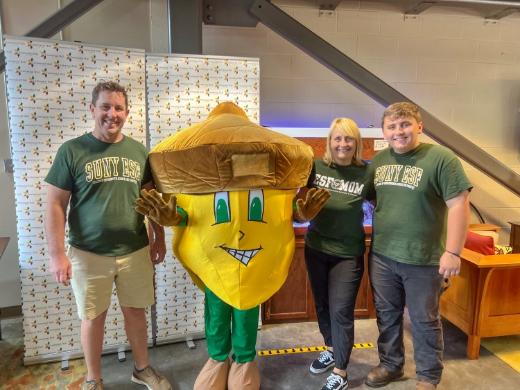 Three people (two parents and their son) stand with a giant acorn mascot that is yellow, green and brown. They are all wearing ESF shirts.